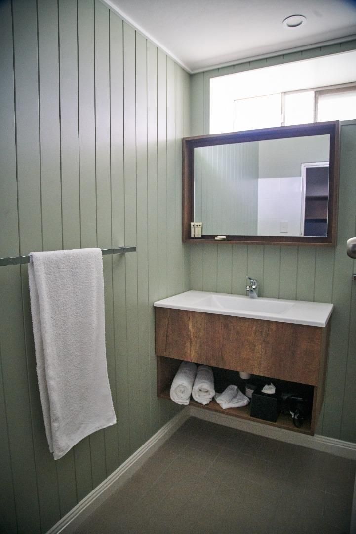 Un baño con tocador de madera, un lavabo blanco, una toalla colgada en un perchero y un espejo sobre el tocador.