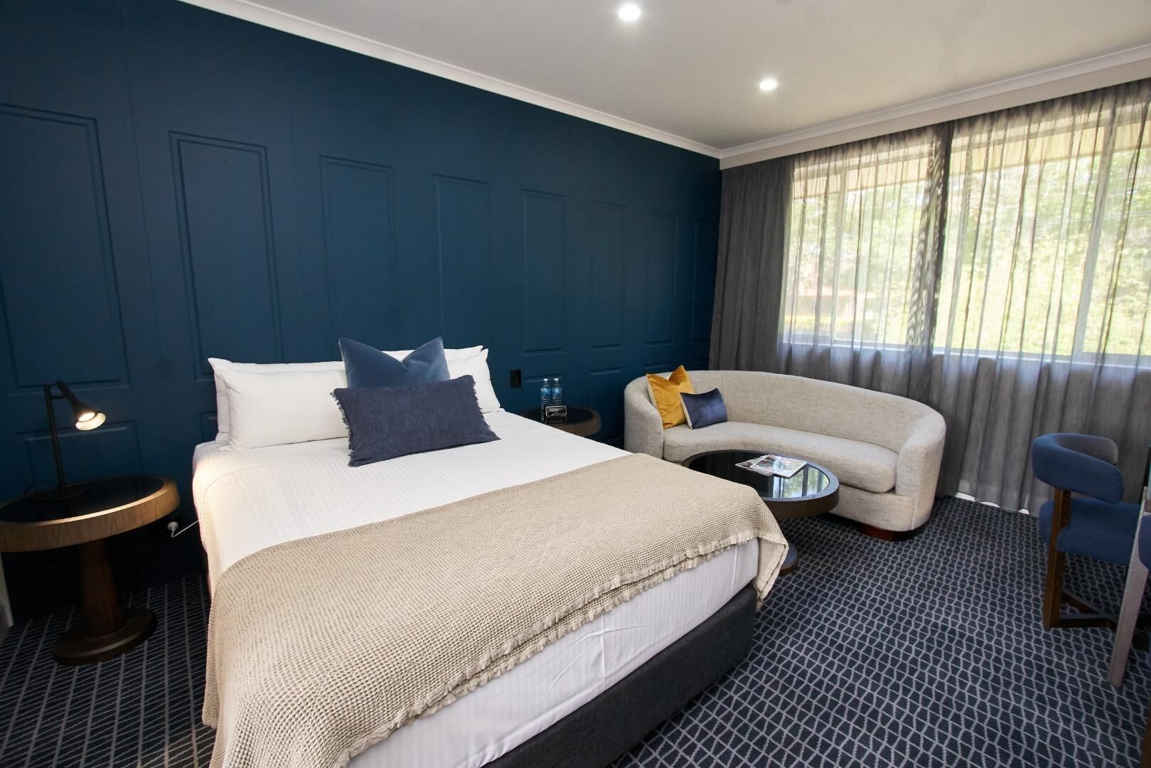 Ein Hotelzimmer mit einem großen Bett, einem Sofa, einem kleinen runden Tisch und einem Fenster mit Vorhängen.