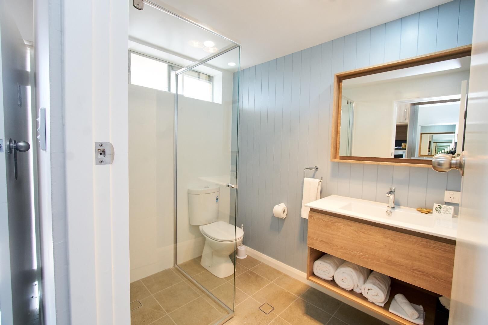 A bathroom with a glass shower enclosure, a toilet, a sink with a mirror, and a towel rack.