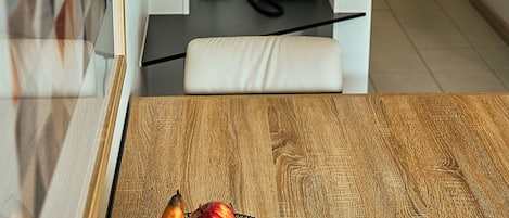 Une table en bois avec un panier de fruits, une chaise blanche, un téléphone et une étagère avec des livres et une plante.