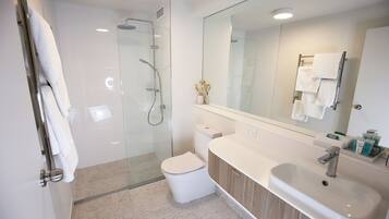 Un baño moderno con ducha de vidrio, inodoro blanco y tocador con lavamanos y espejo.