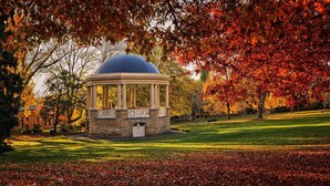 Un belvédère en pierre surmonté d’un dôme, entouré d’un parc aux couleurs automnales.