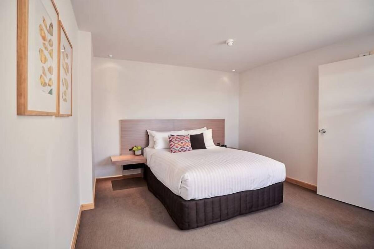 Quarto com cama, mesa de cabeceira e apoio para objetos pessoais.
