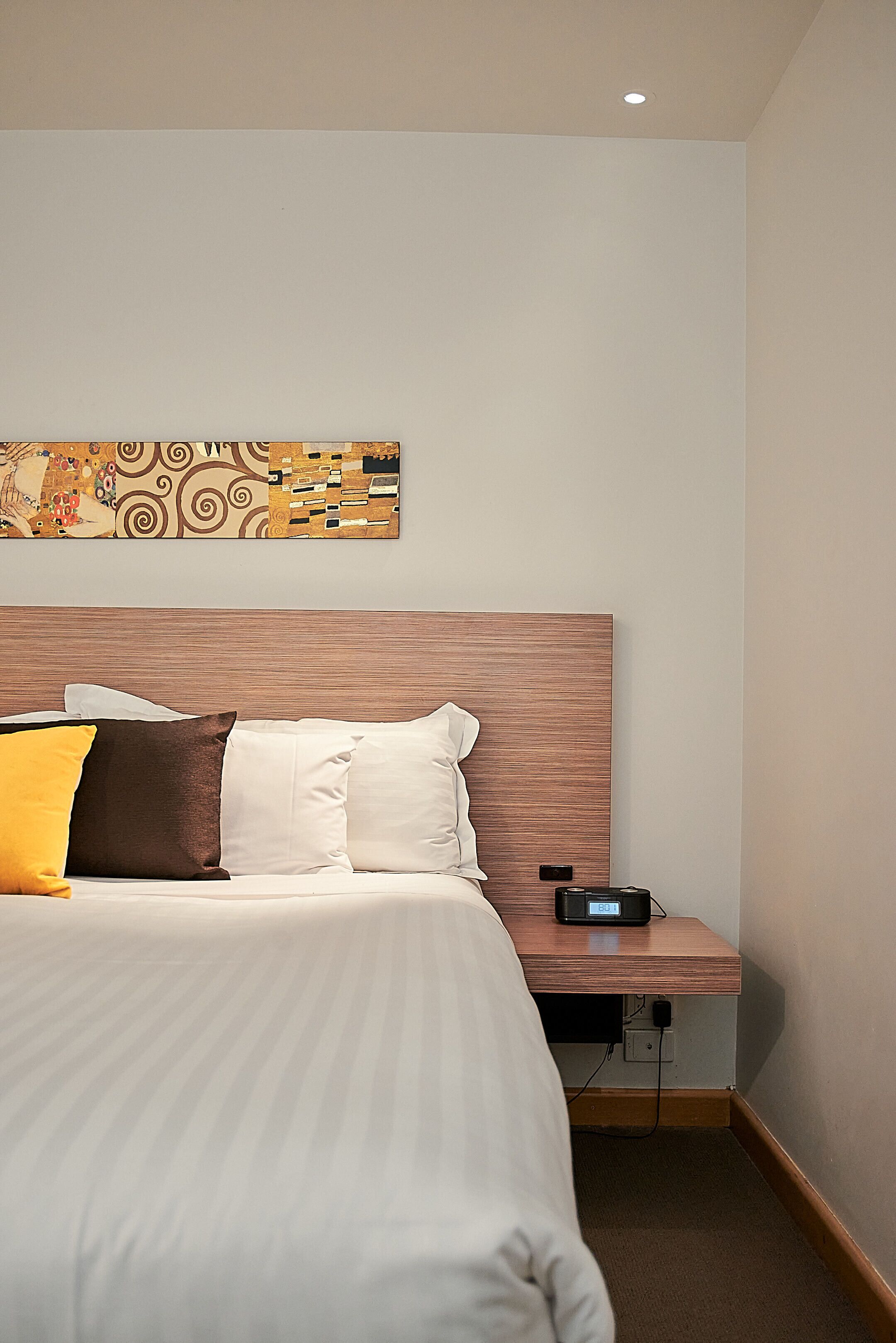 A neatly made bed with white and brown bedding, a wooden headboard, and a bedside table with a power outlet.