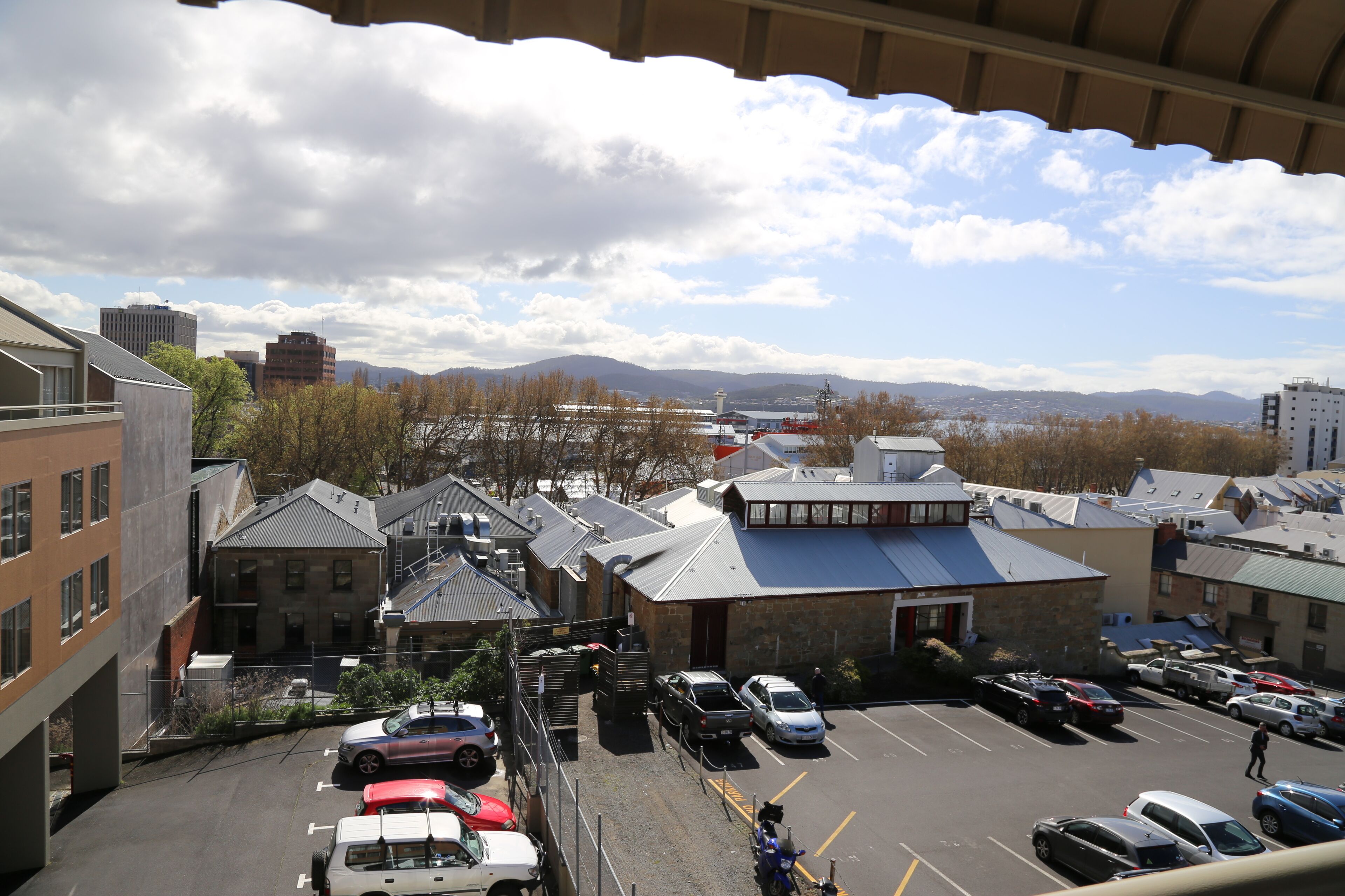 A parking lot with several cars, a building with a blue roof, and a view of mountains in the background.