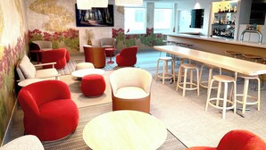 Un espace lounge moderne avec des fauteuils rouges et beiges, un long bar en bois et un grand tableau accroché au mur.