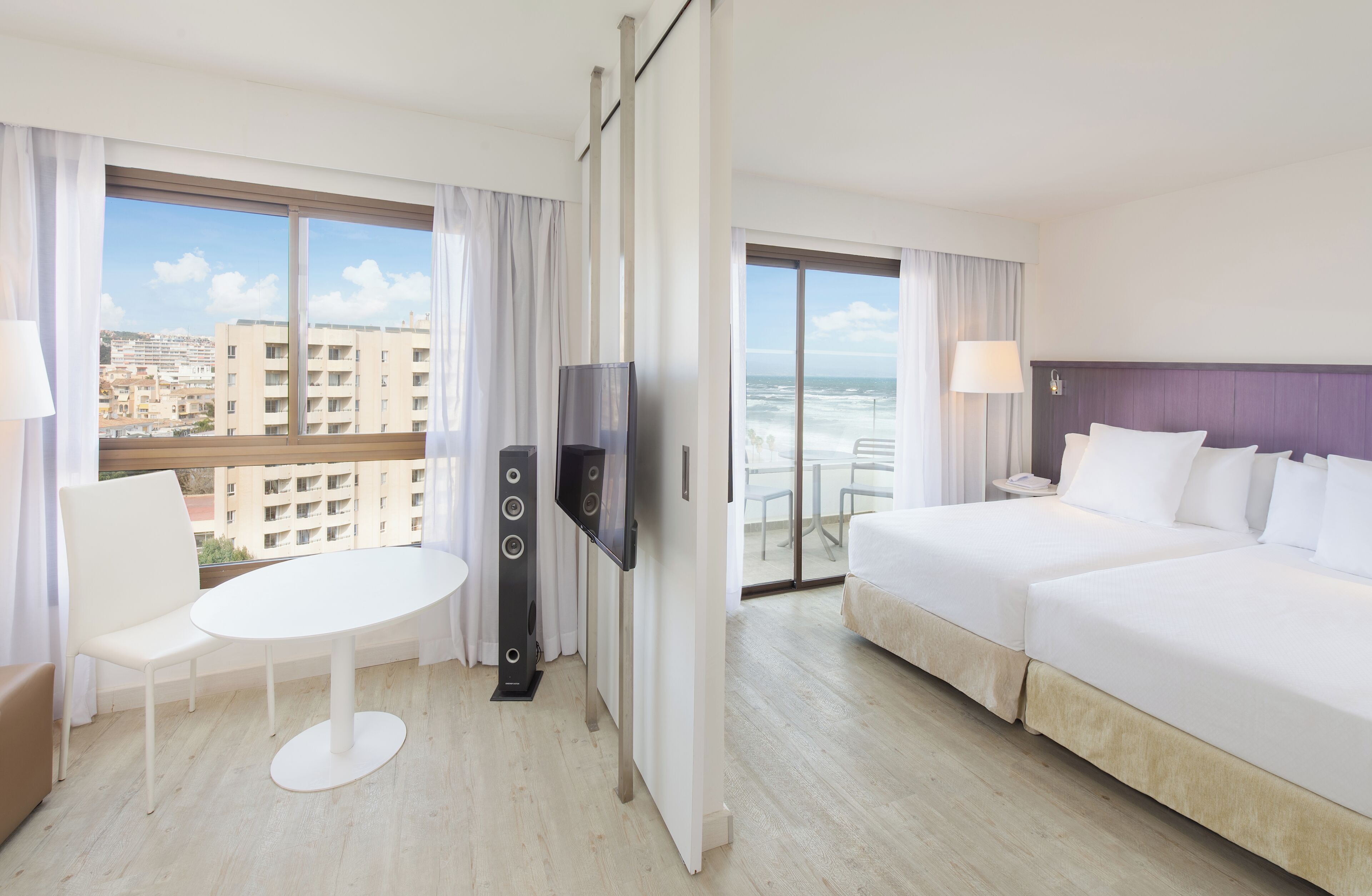Habitación de hotel con balcón, televisión, cama, mesa y una silla.