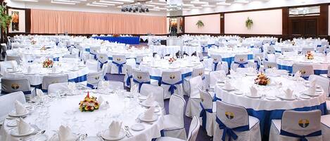 A banquet hall with round tables set for events, each with white tablecloths and blue sashes.