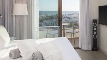 Une chambre d’hôtel avec un grand lit, une télévision, un haut-parleur et un balcon offrant une vue sur la ville et la mer.