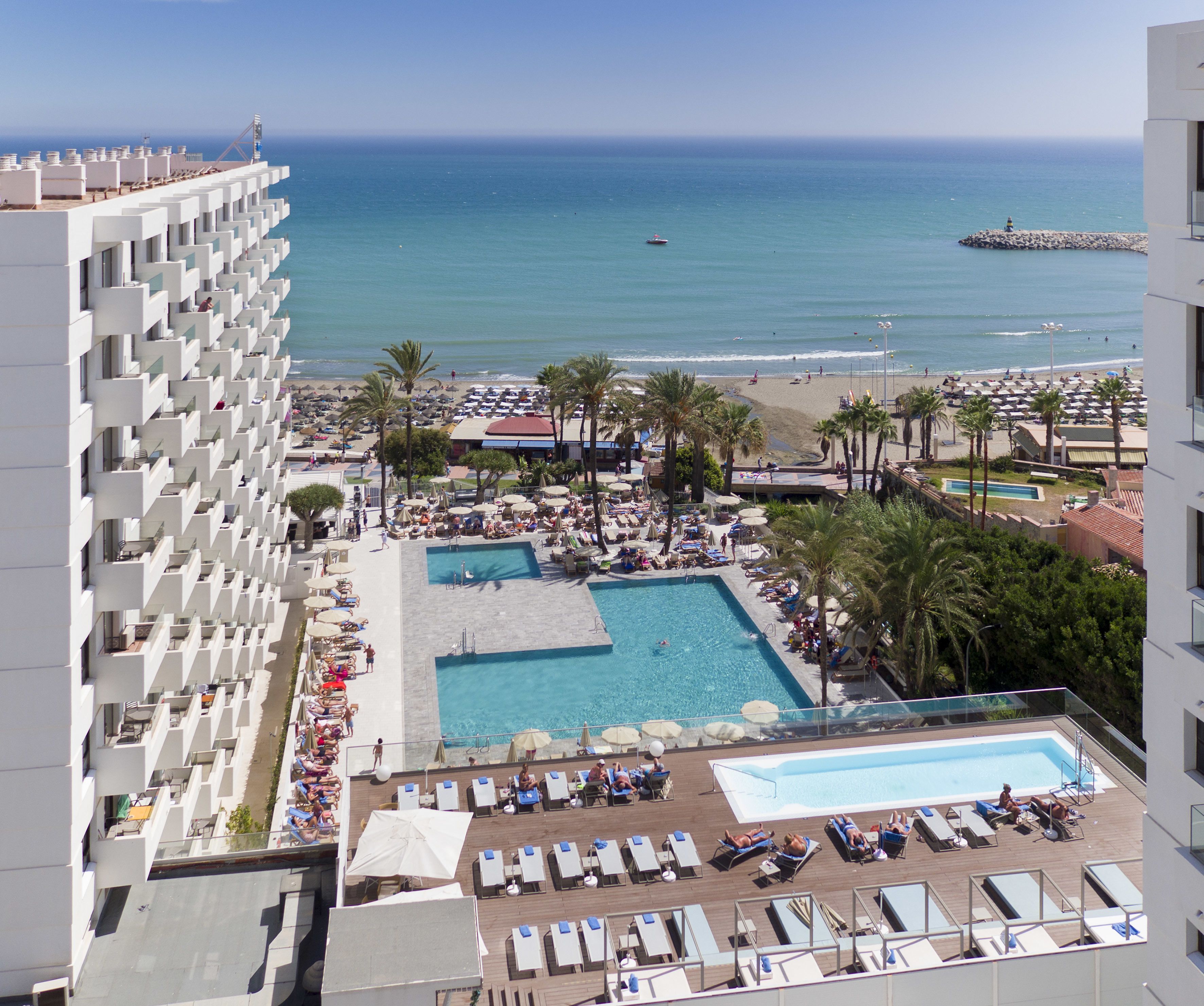 A resort with a large pool, sun loungers, and a view of the beach and ocean.