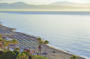 A beach with rows of umbrellas and lounge chairs, a lifeguard tower, and palm trees. - Ocean House Costa del Sol by Grupotel (Torremolinos)