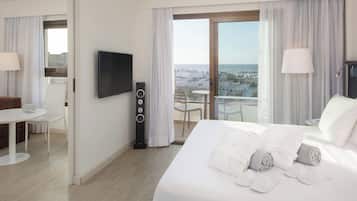 Ein Hotelzimmer mit Bett, Fernseher, Schreibtisch mit Laptop, Lautsprecher und einem Balkon mit Blick auf die Stadt.