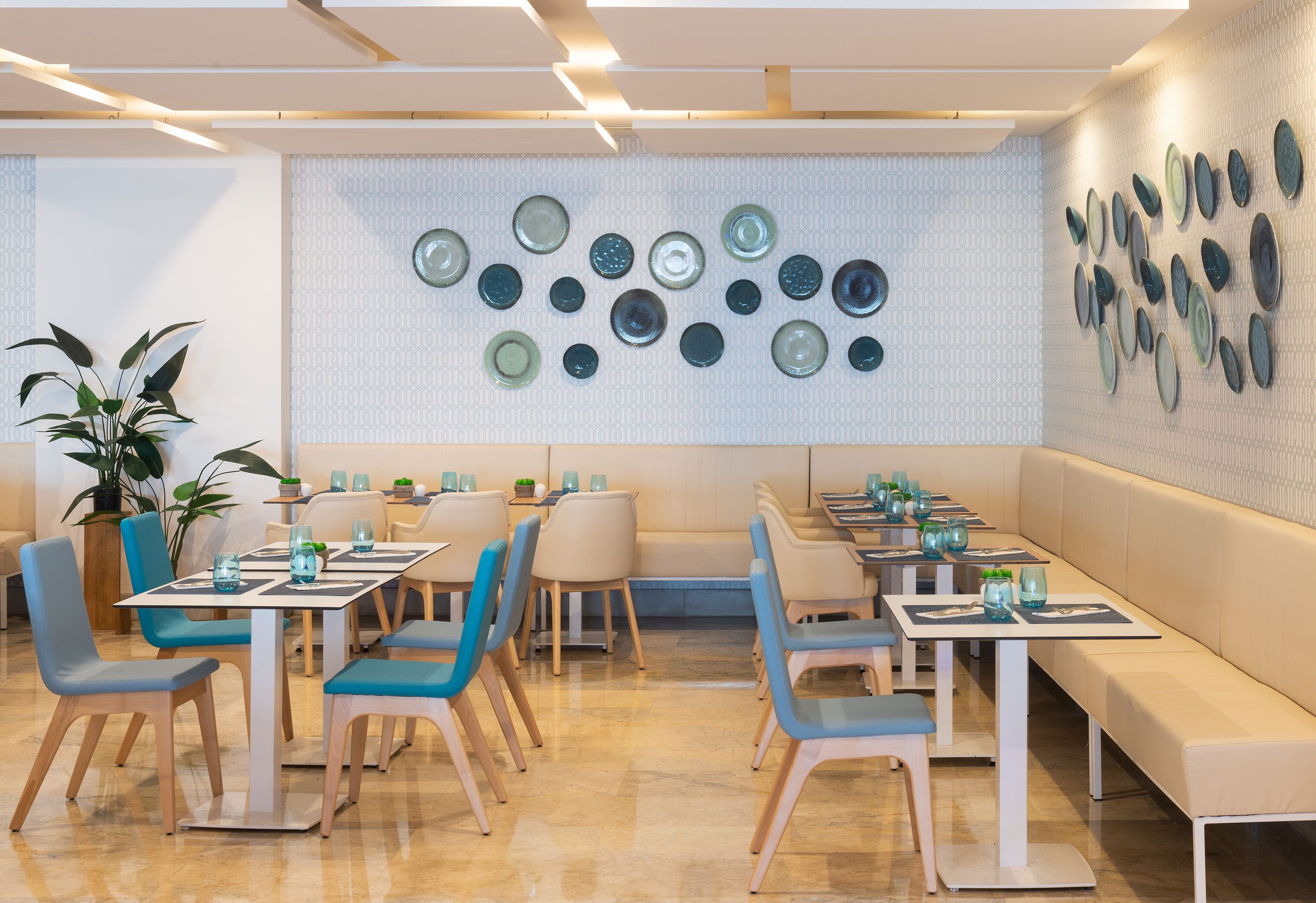 A modern restaurant interior with a long counter, blue chairs, and a wall decorated with plates.