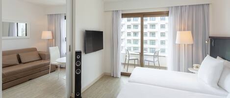 A hotel room with a bed, a sofa, a TV, a desk, and a balcony with curtains.