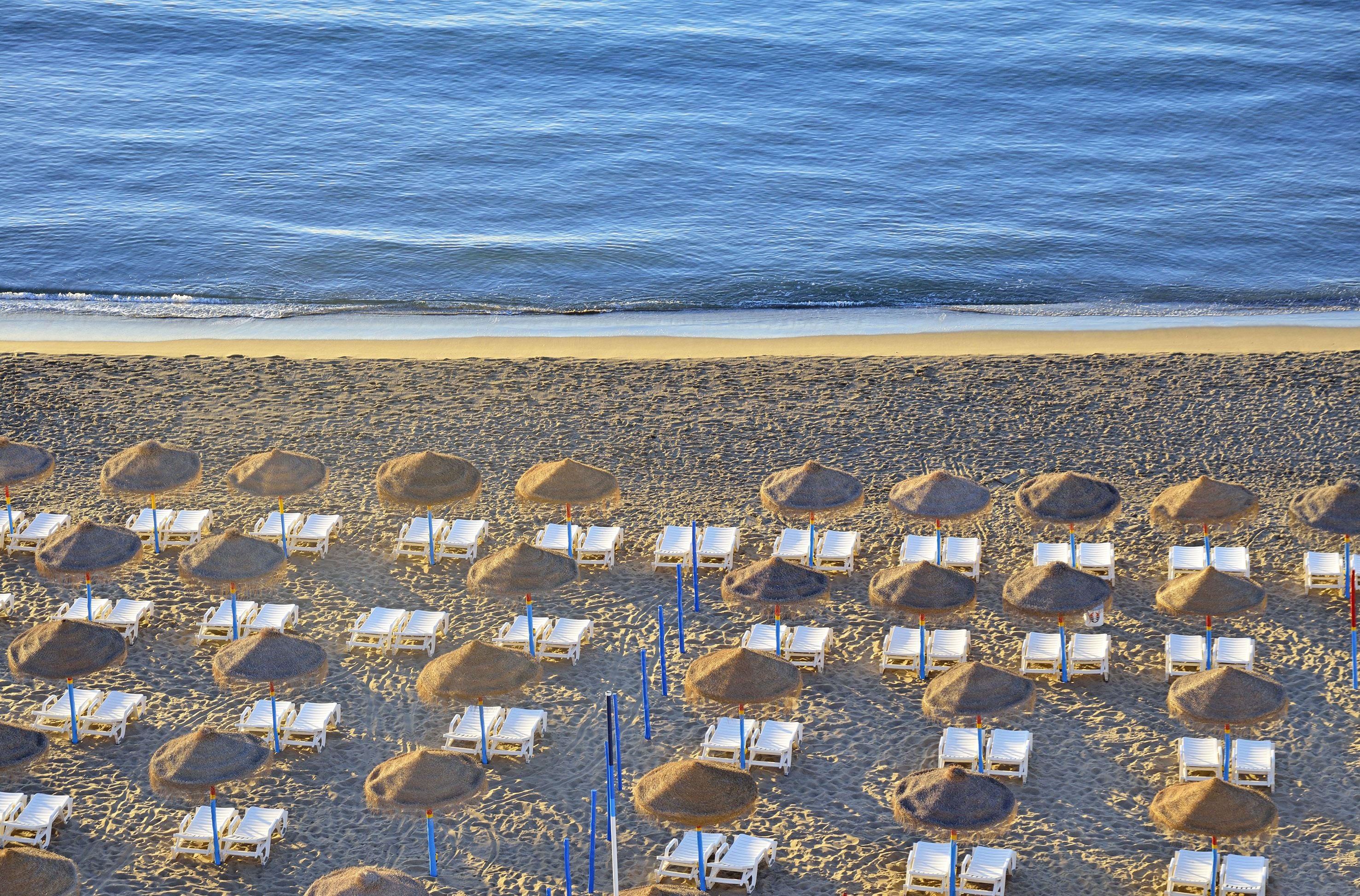 Ein Strand mit Liegestühlen und reetgedeckten Sonnenschirmen.