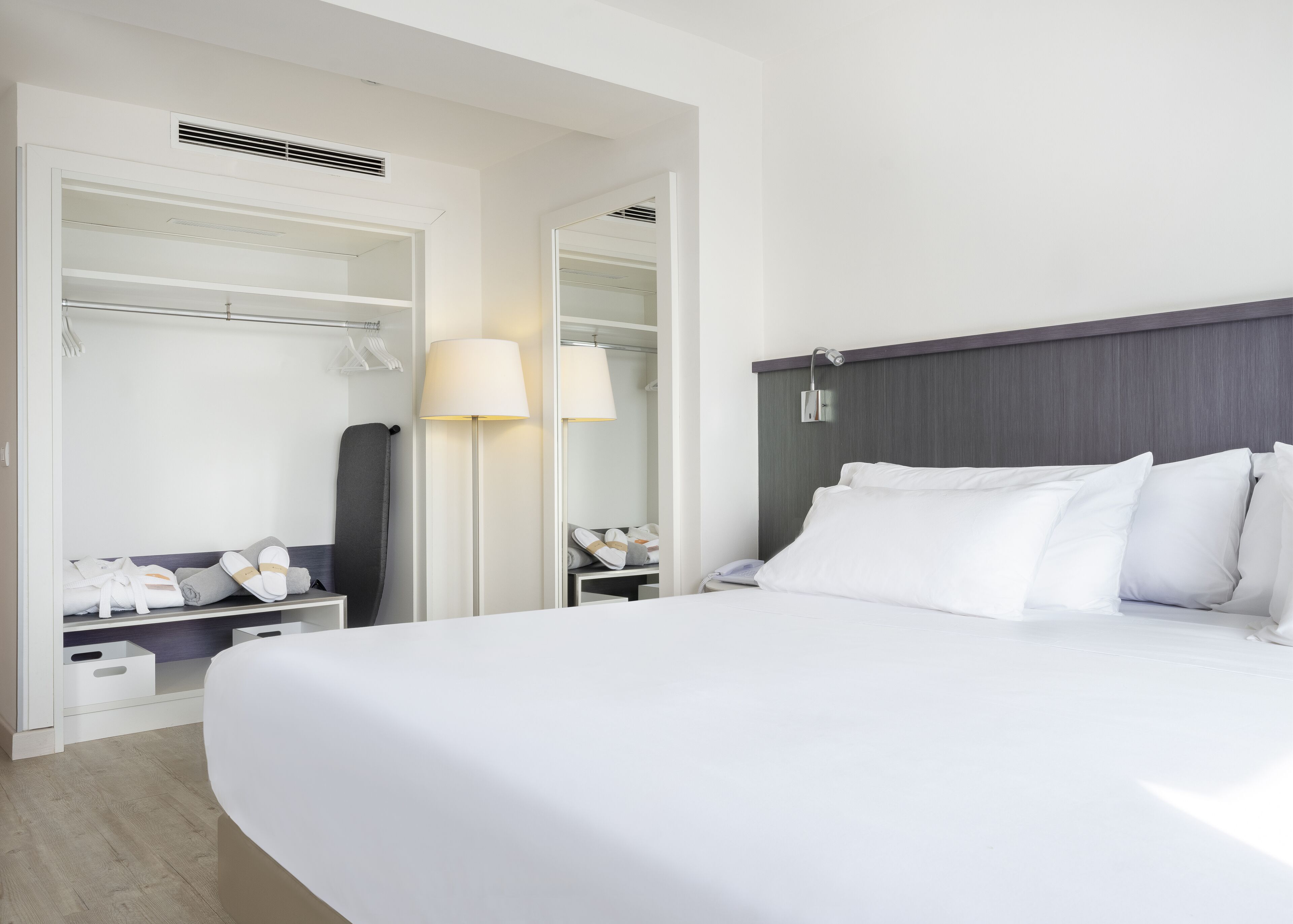 Une chambre d’hôtel avec un grand lit, une armoire, une table de chevet avec une lampe et un miroir.