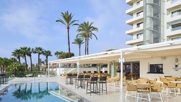 Un espace aménagé au bord de la piscine, avec des chaises et des tables, un bar et un bâtiment doté de balcons.
