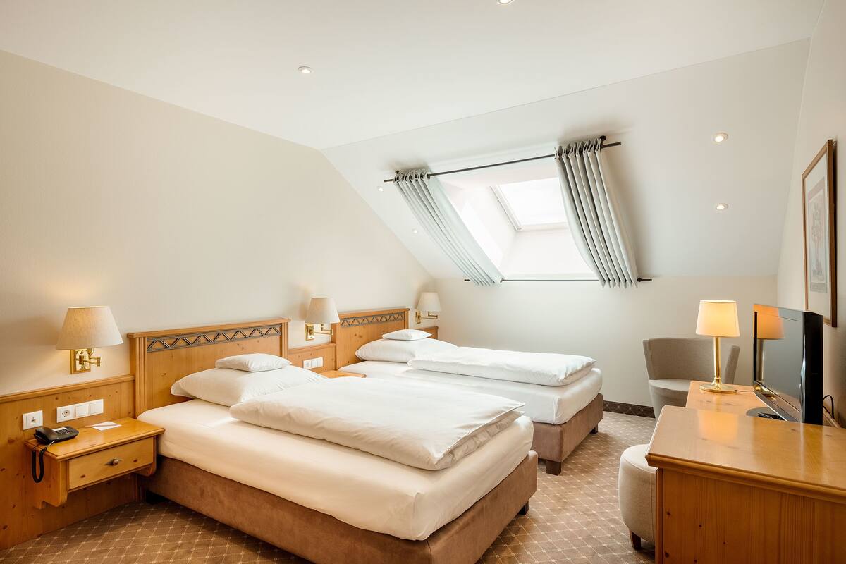 A hotel room with two beds, a desk, a chair, and a TV.