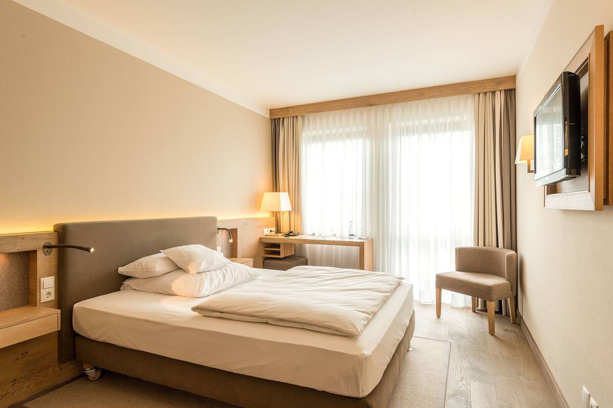 A hotel room with a bed, a desk, a chair, a TV, and a window with curtains.