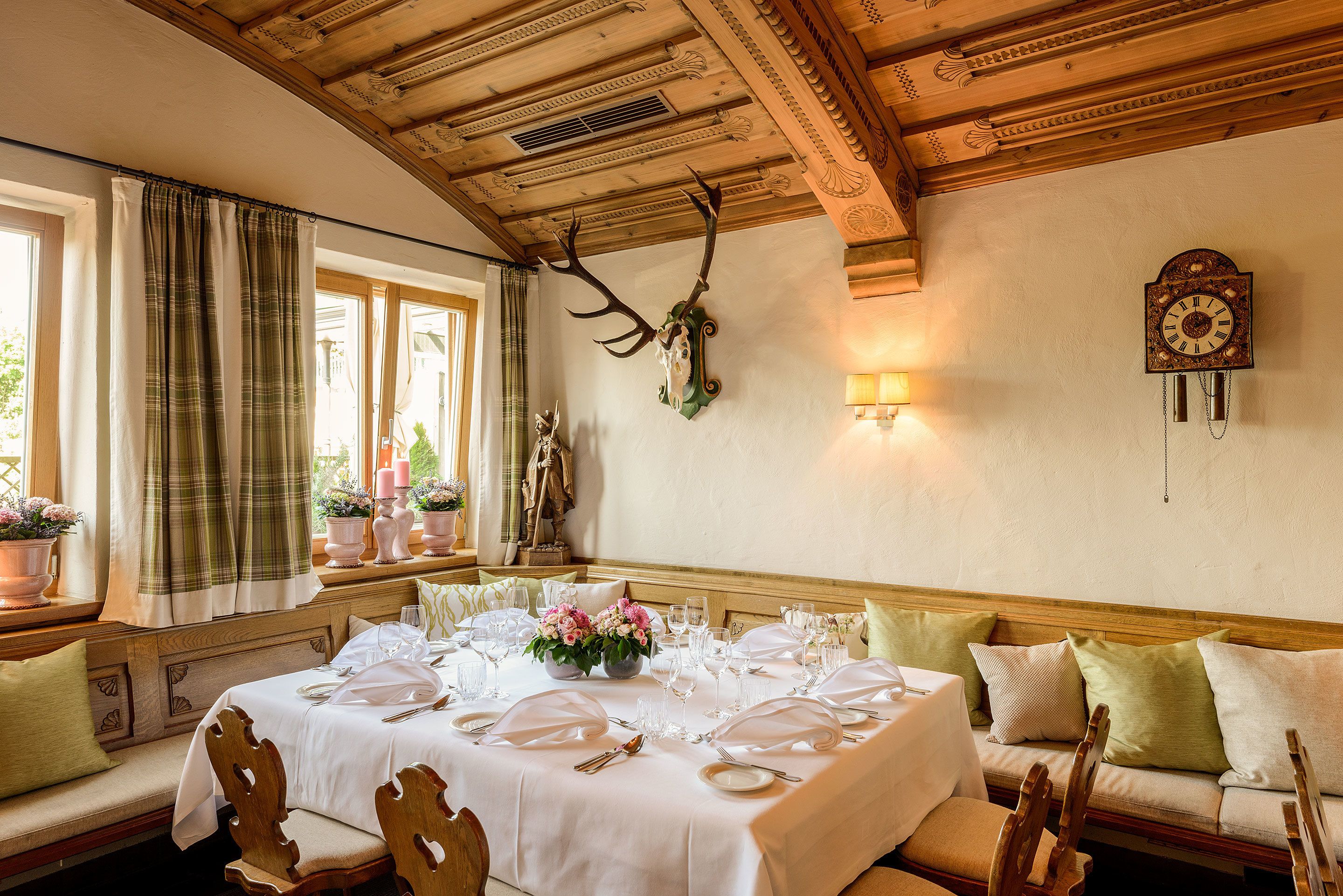 A dining room with a large table set for a meal, wooden ceiling beams, and a wall-mounted clock.