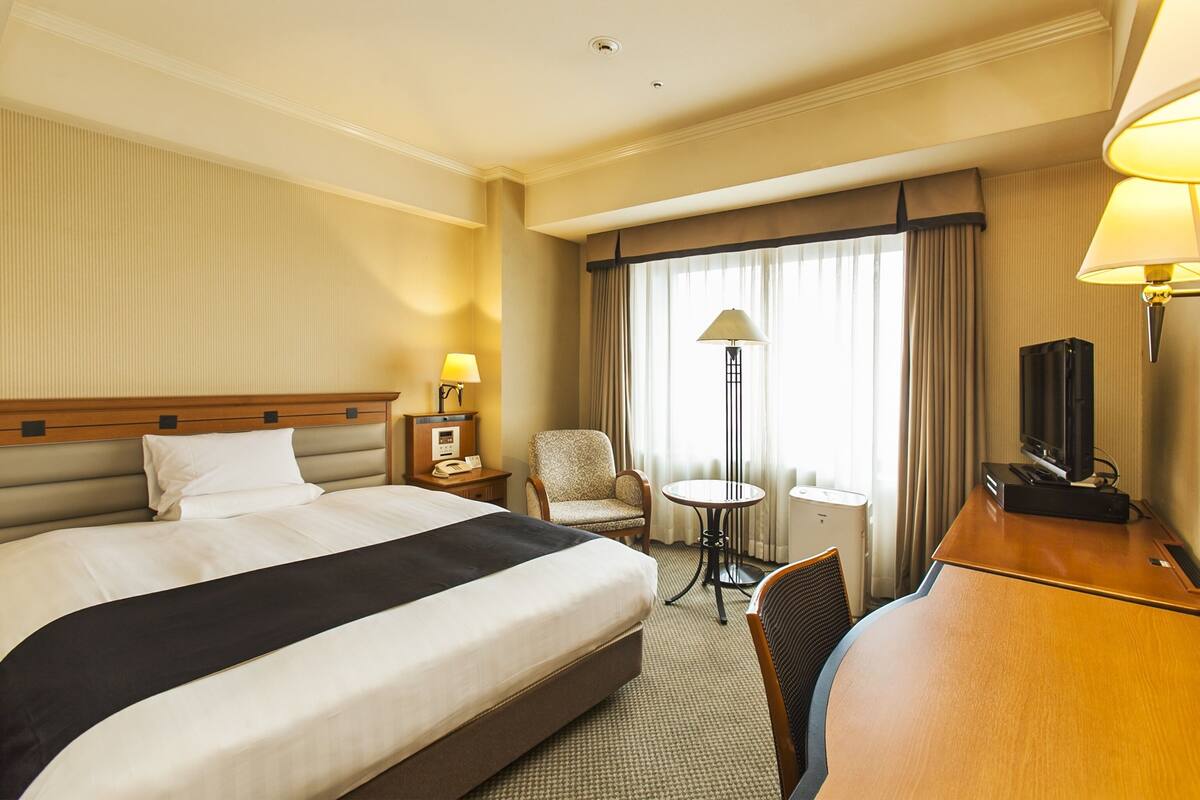 Une chambre d’hôtel avec un grand lit, un bureau avec une télévision, une chaise, une petite table et une lampe.