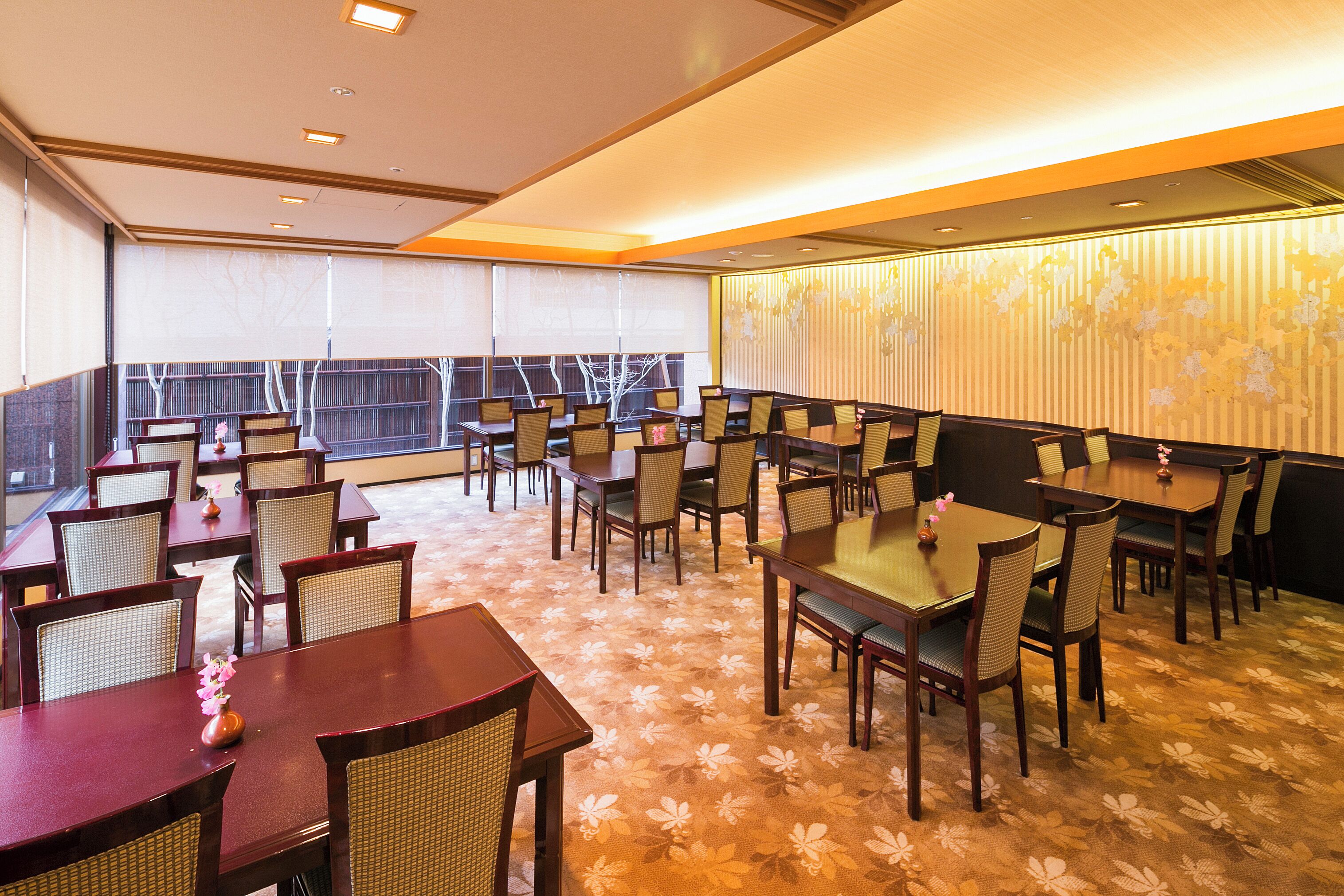 Un vaste espace dédié à la salle à manger, avec de nombreuses tables et chaises, de grandes fenêtres et un mur décoratif.