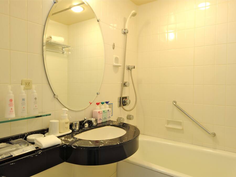 A bathroom with a black sink, white tiles, a glass shelf with toiletries, a handheld showerhead, and a grab bar.