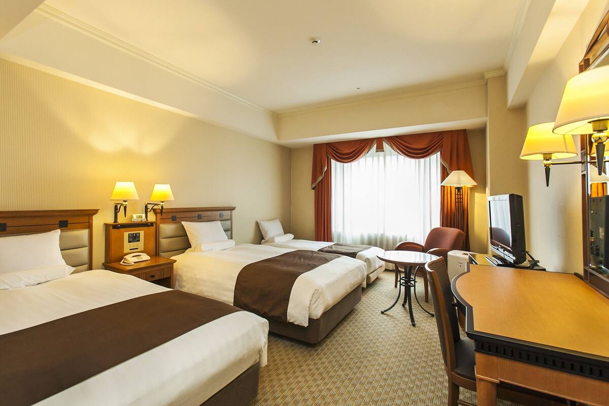 Une chambre d’hôtel avec trois lits, un bureau, une chaise et un téléviseur.
