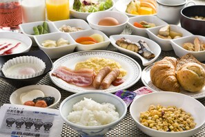 Enjoy a hearty breakfast spread with eggs, bacon, sausages, croissants, rice, and corn, along with a variety of sides.