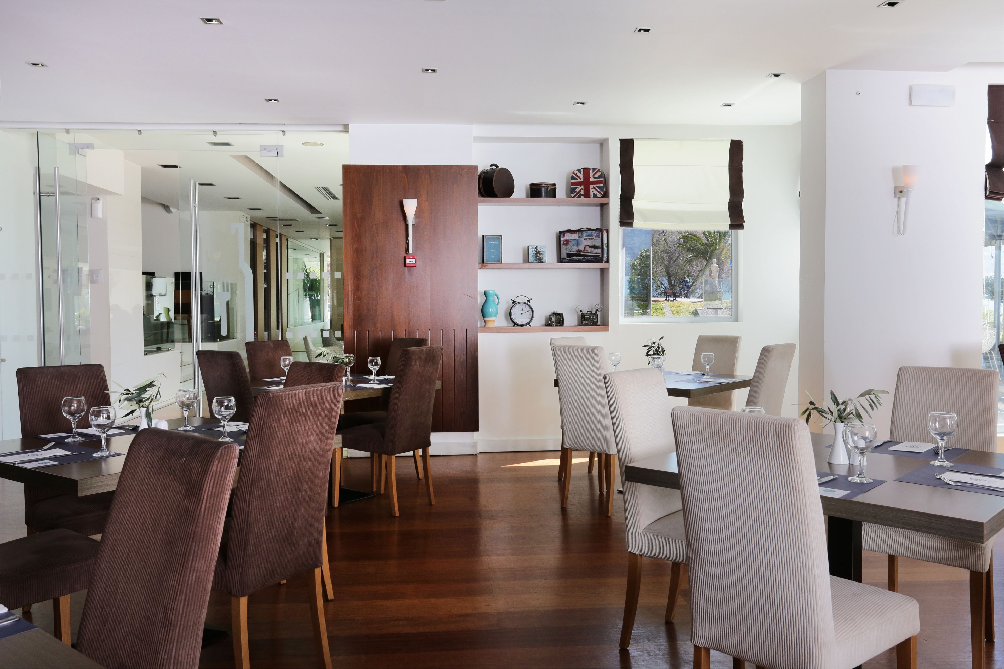 A modern dining area with wooden flooring, dark and light brown upholstered chairs, and glass partitions.