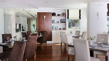 A modern dining area with wooden flooring, dark and light brown upholstered chairs, and glass partitions.