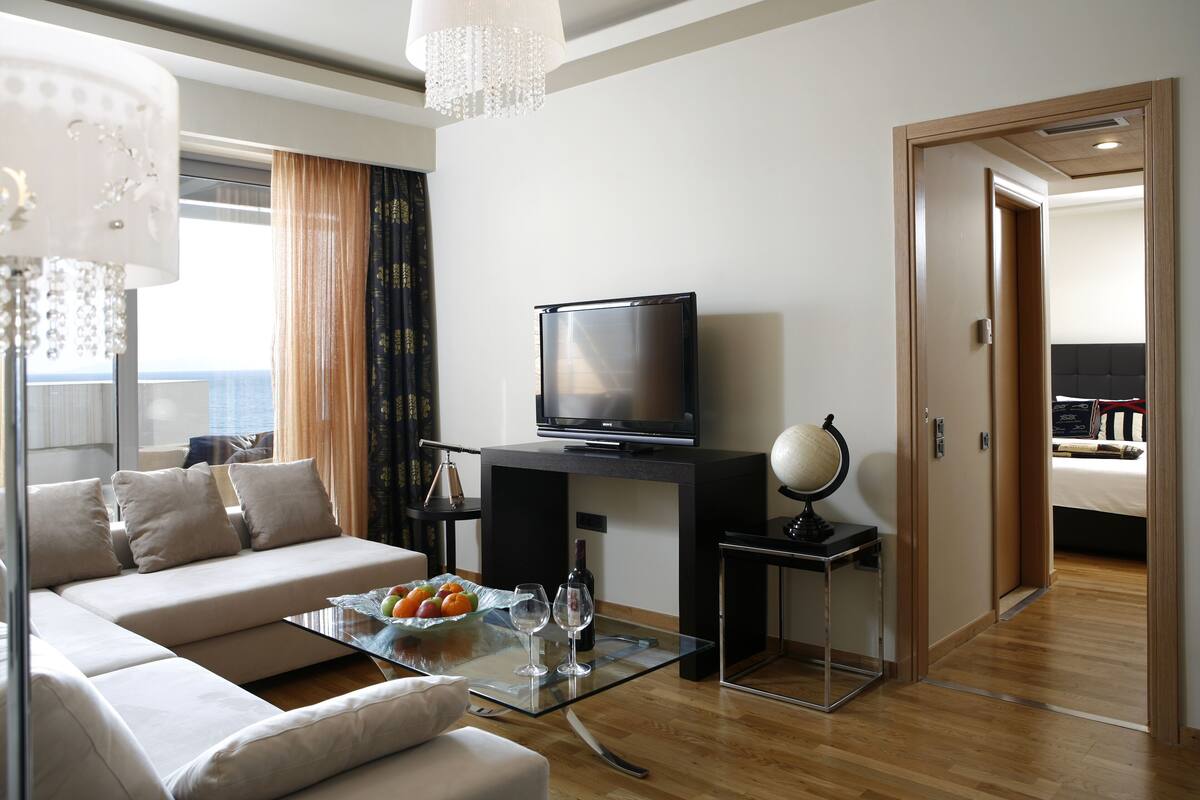 Una sala de estar moderna con un sofá, una mesa de centro de vidrio con frutas y copas de vino, un televisor de pantalla plana, un globo terráqueo y piso de madera.