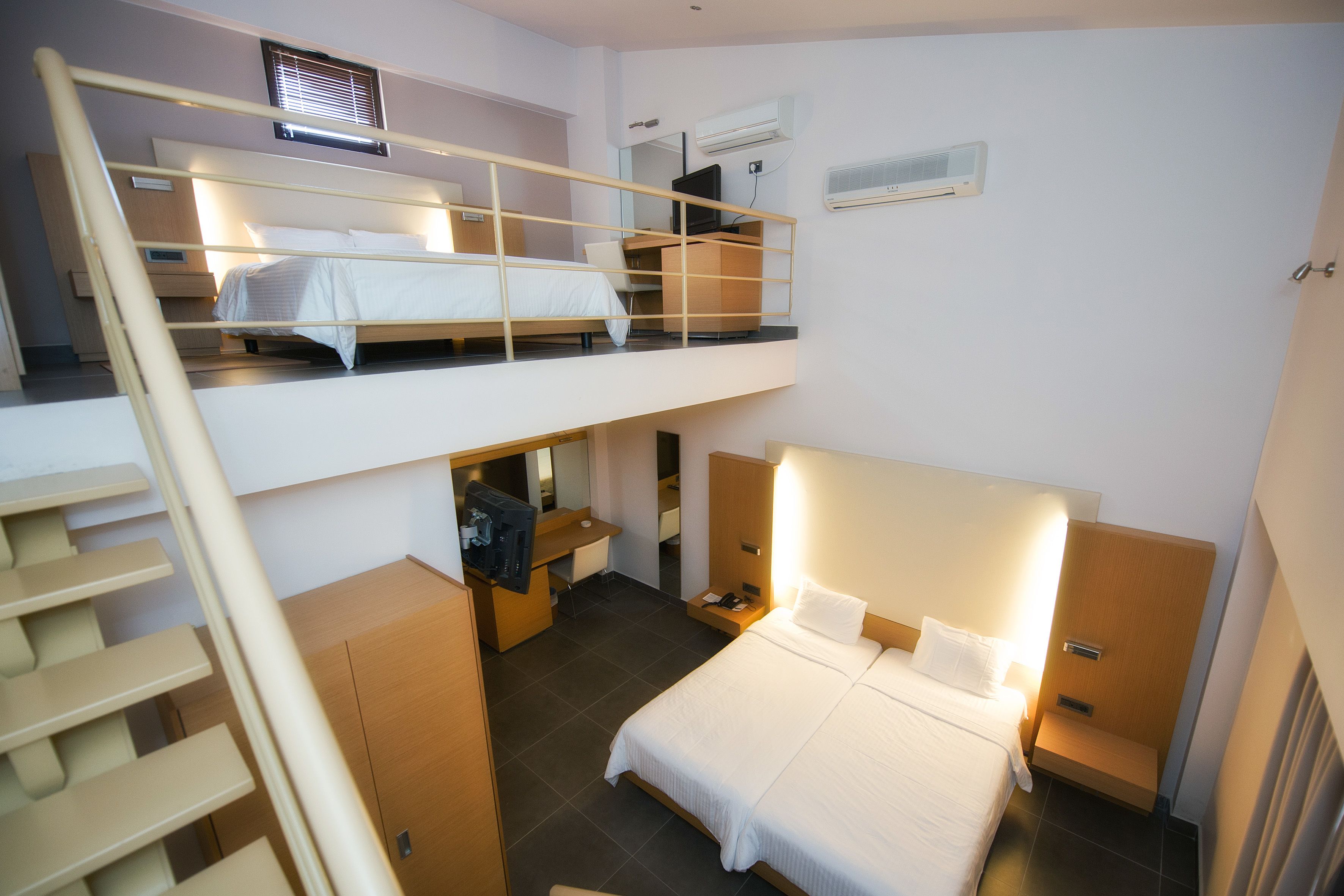 Une chambre à deux niveaux, avec un lit superposé à l’étage supérieur et un lit simple à l’étage inférieur. On y trouve un bureau avec une chaise, une armoire et une petite table avec une lampe.