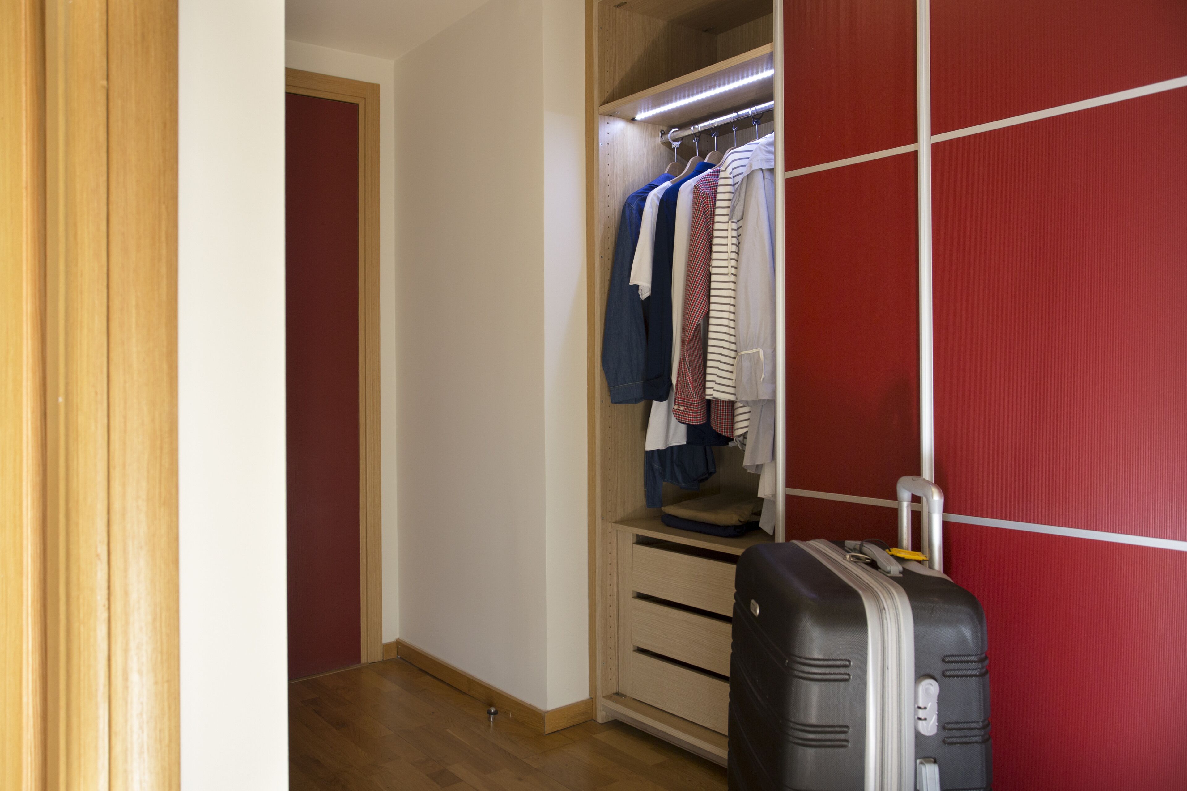A walk-in closet with hanging clothes and a suitcase.
