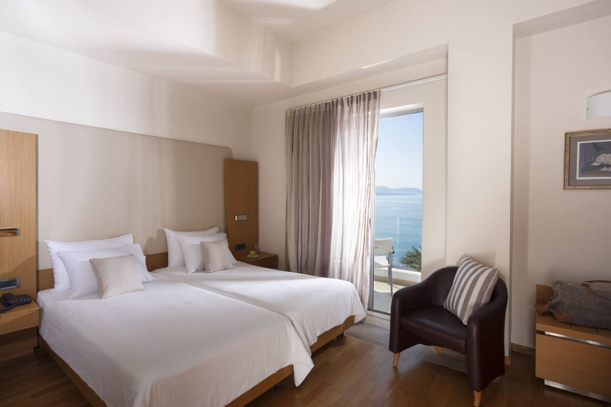 Habitación de hotel con dos camas, una silla, un escritorio y vista al mar.