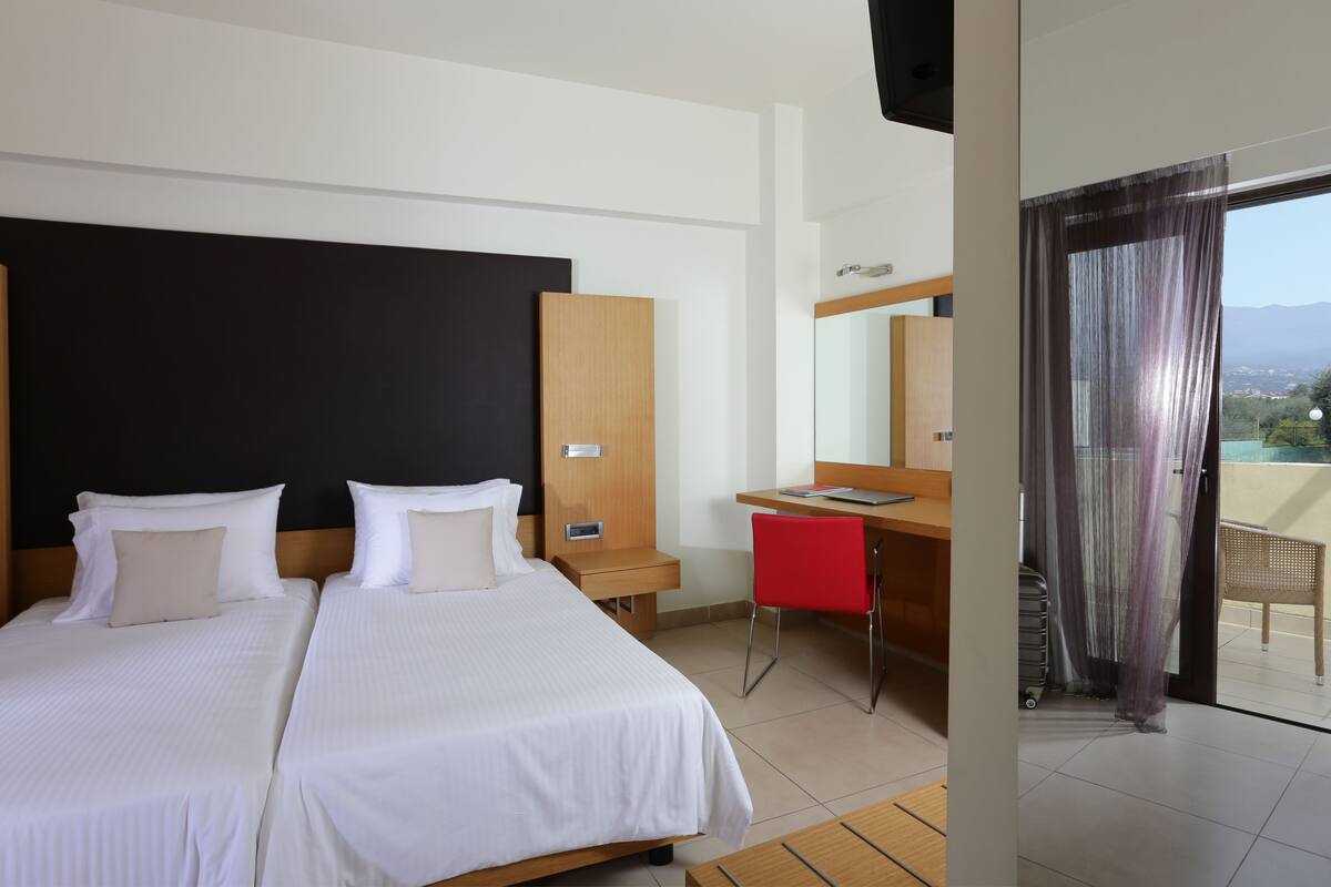 Habitación de hotel con dos camas, un escritorio, una silla y un balcón con vistas.