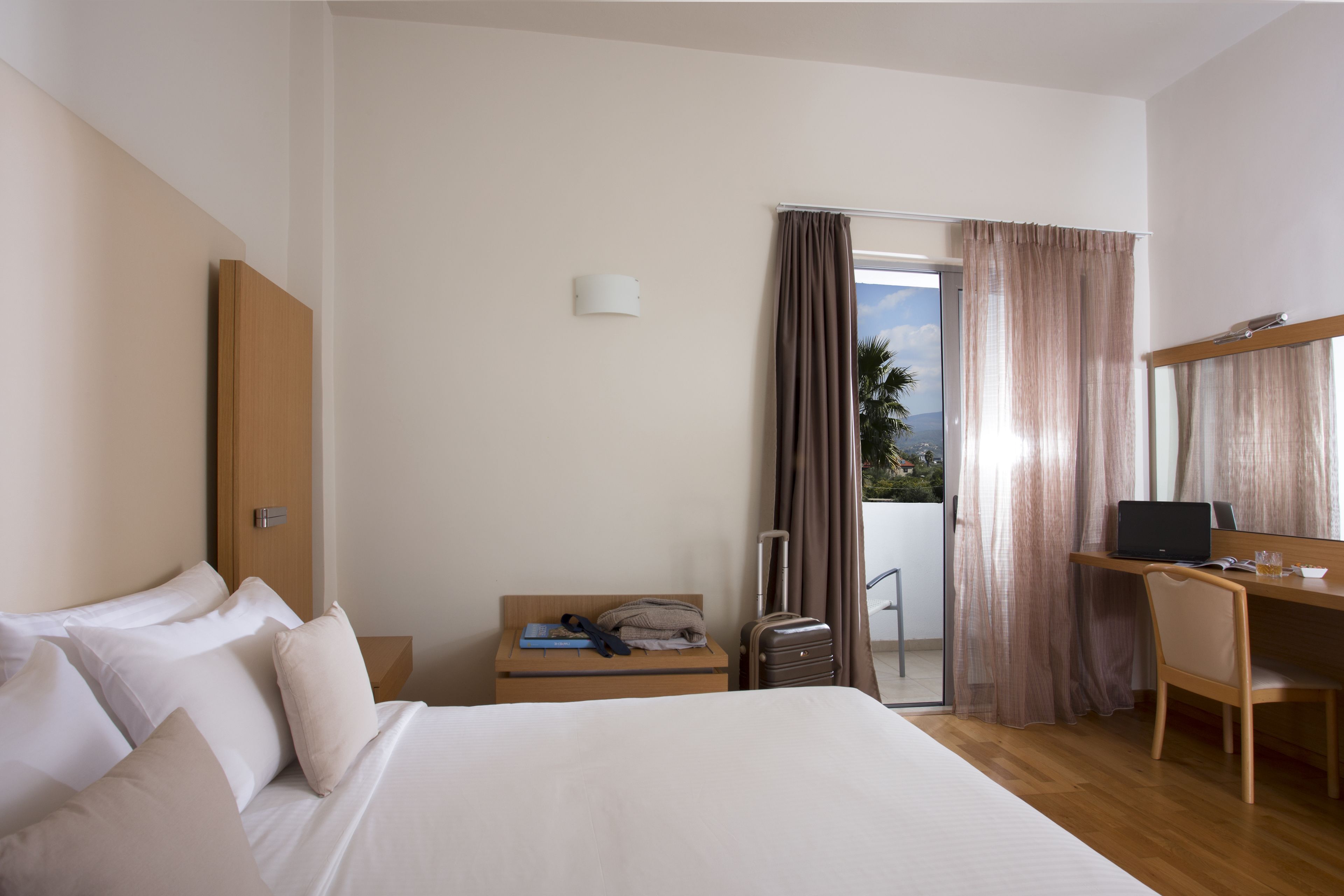 A hotel room with a bed, a desk, a chair, a suitcase, and a door leading to a balcony.