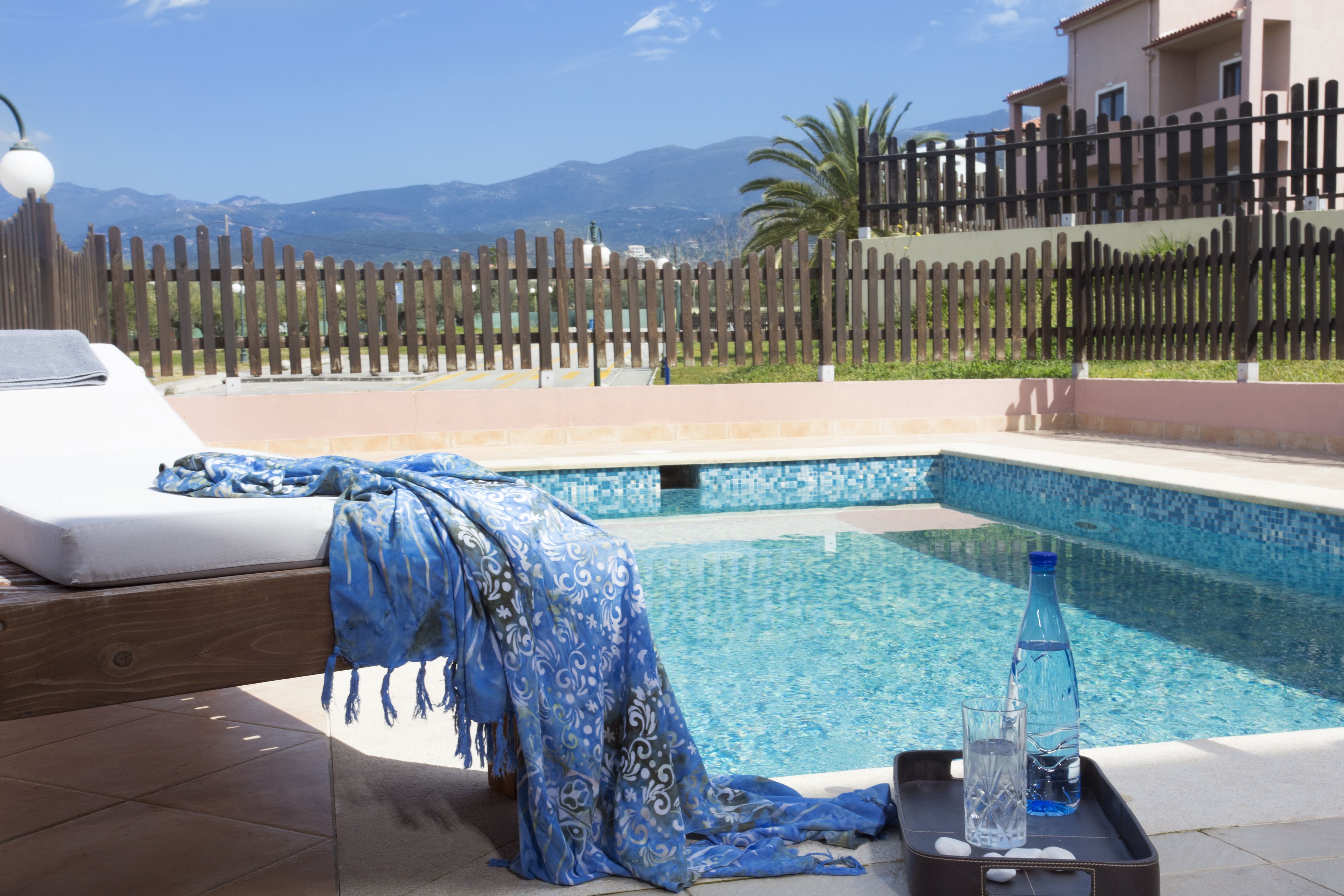 Zona junto a la piscina con una cama, una toalla y una bandeja con una botella y un vaso.
