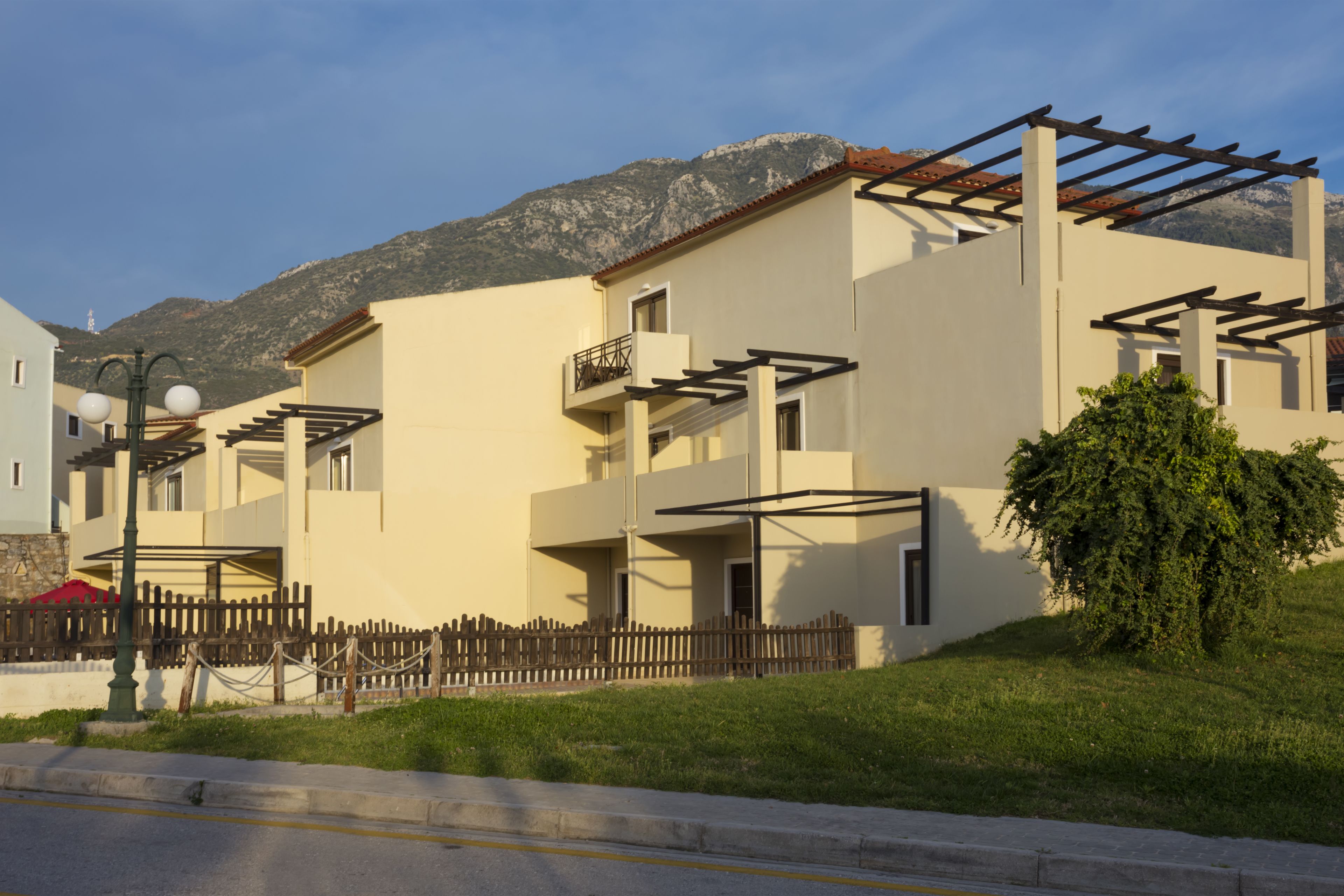 A modern building with balconies, a wooden fence, and a mountain backdrop.