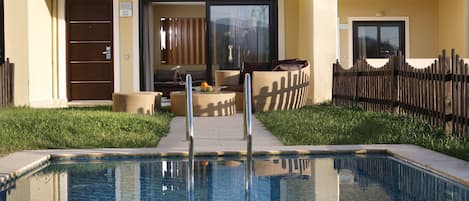 A swimming pool with a glass barrier, a wooden fence, and a building entrance with a door and a window.