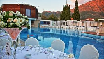 A poolside dining area with tables set for a meal, a large floral arrangement, and a mountain backdrop.