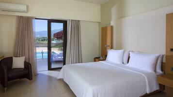 A hotel room with a large bed, a chair, a nightstand, and a view of a pool and mountains.