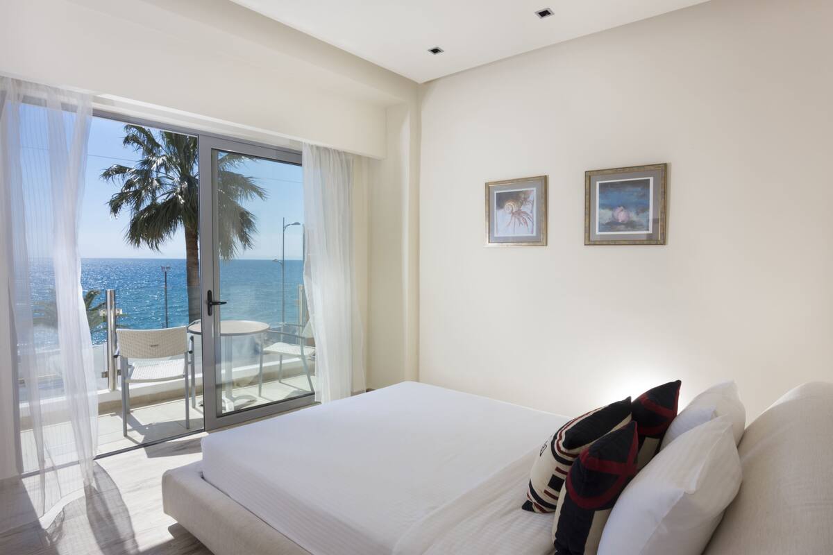 Una habitación de hotel con cama, balcón con vista al mar y dos cuadros en la pared.