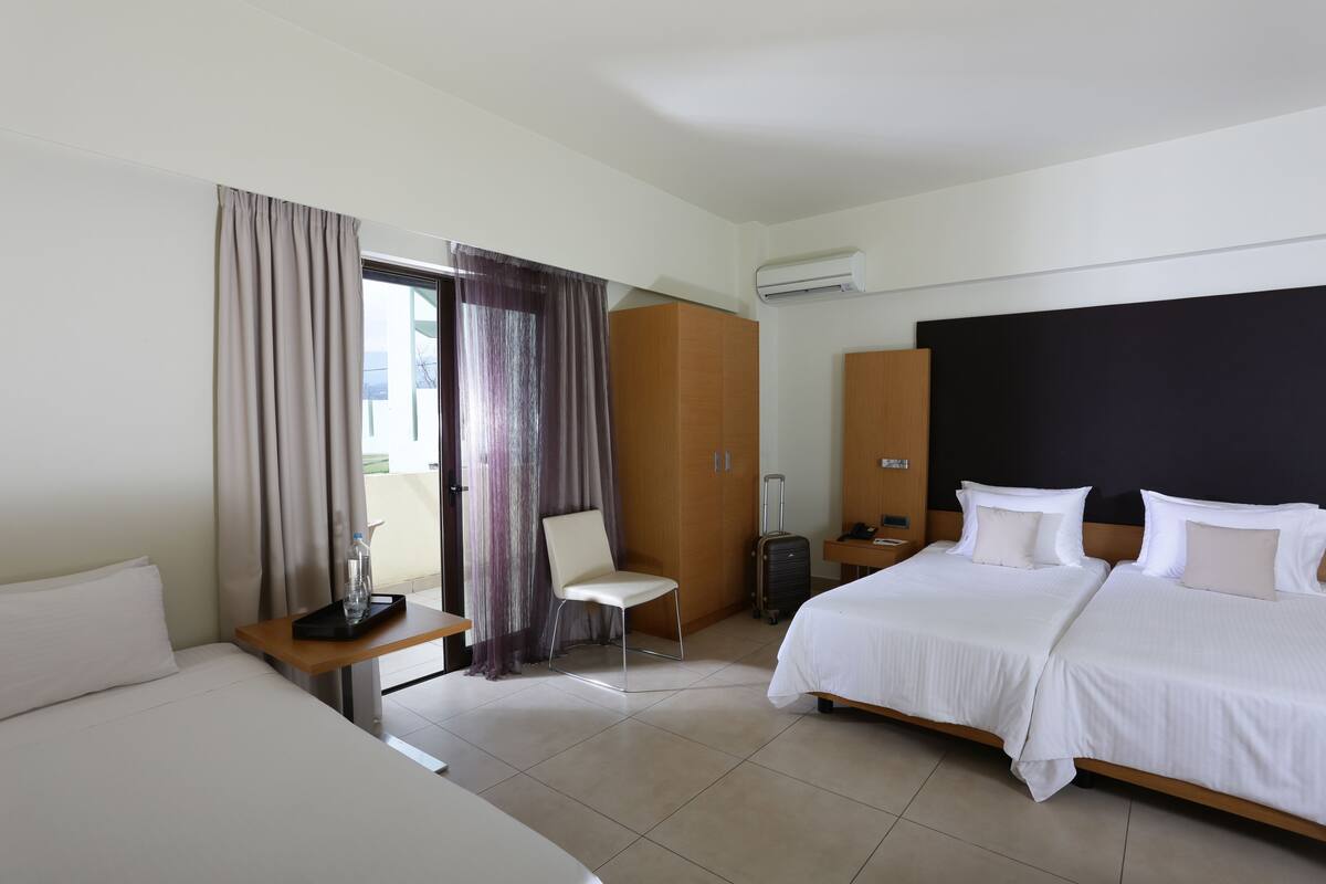 Habitación de hotel con una cama grande, una cama más pequeña, un escritorio con silla, una maleta y un armario.