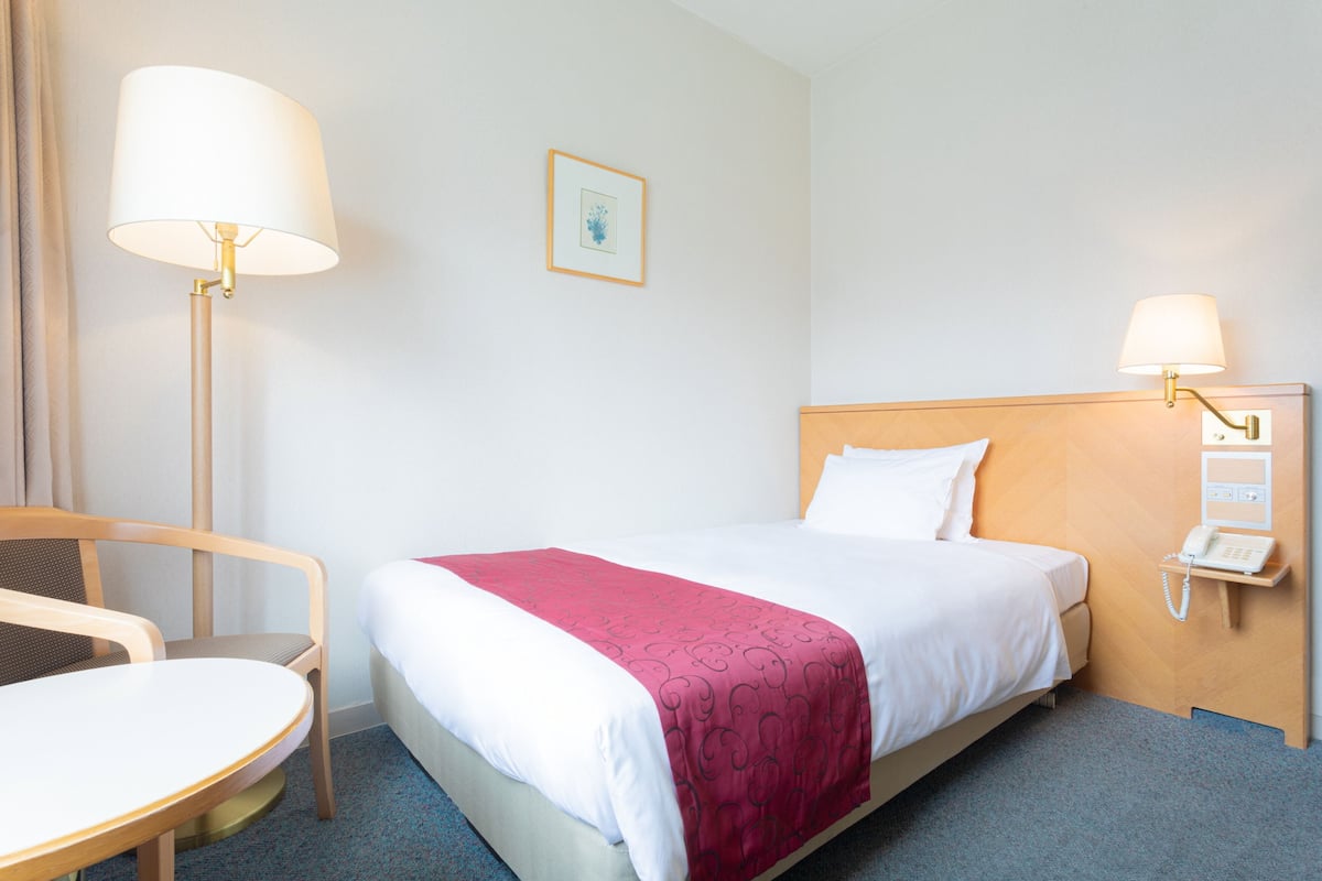 A hotel room with a bed, a desk, a chair, a lamp, and a telephone.