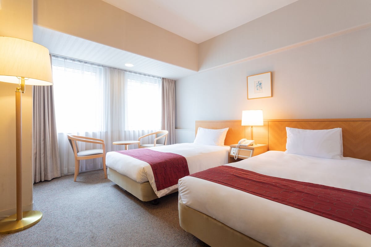 A hotel room with two beds, a chair, a desk, and a lamp.