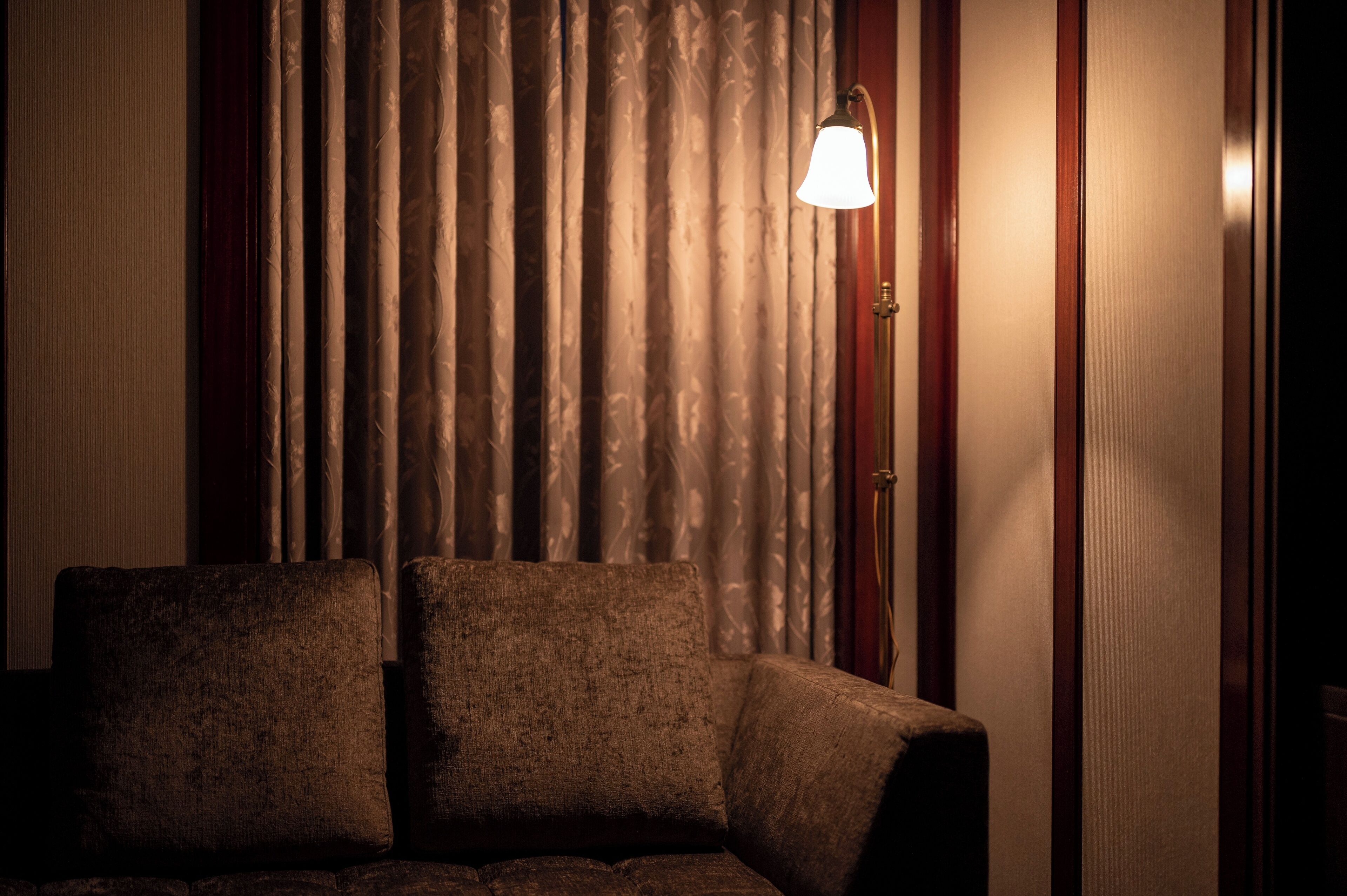 A room with a dark-colored armchair, a lamp, and a curtain.
