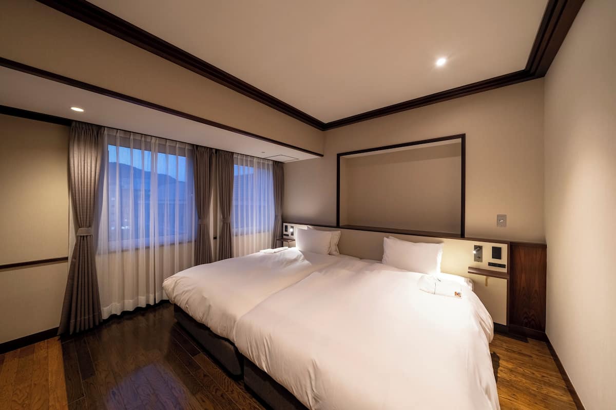 A hotel room with a large bed, a flat-screen TV, wooden flooring, and a window with curtains.