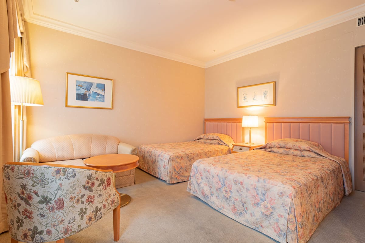 A hotel room with two beds, a sofa, a small table, and two lamps.