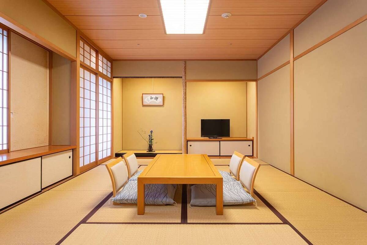 A traditional Japanese room with tatami flooring, a low wooden table, and a television on a stand.